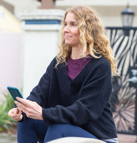 A woman sits outside while calmly reviewing her loan information on her cell phone.