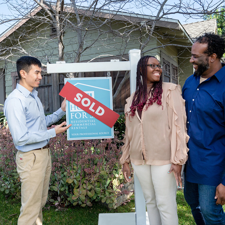 A couple, along with their realtor, stands outside their new home