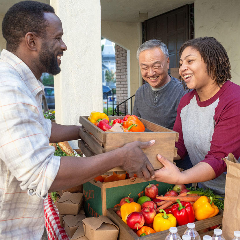 Three people exchange fresh produce while volunteering for a local nonprofit organization, helping community food distribution.