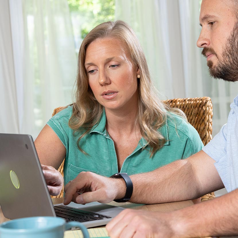 A woman and a man are seated while reading TruStage™ financial wellness education program materials from a tablet.