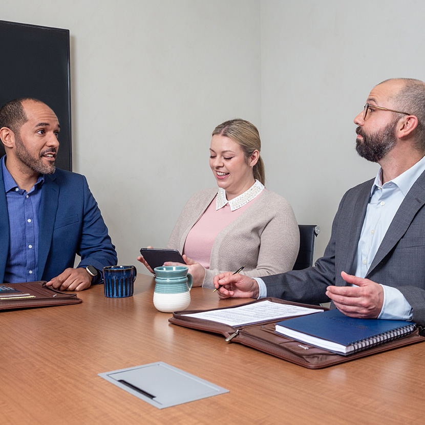 A group of employees in a conference room discuss their retirement program from TruStage™