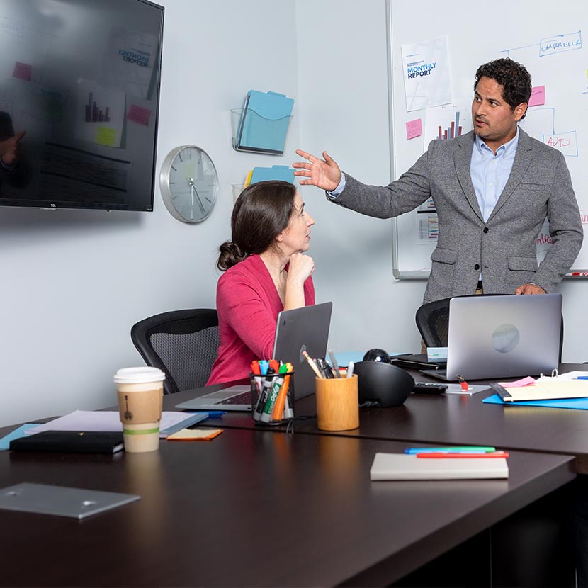 Two employees in an office with TV and whiteboard discuss the Workplace Solutions program from TruStage™