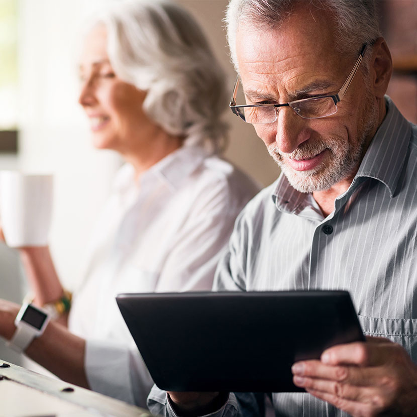 An older couple use a tablet to review IRS Cost-of-Living Adjustment (COLA) for 2025 over morning coffee.